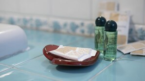 Une salle de bain avec un sol carrelé de bleu, un porte-savon rouge contenant un savon, et deux bouteilles de shampoing.