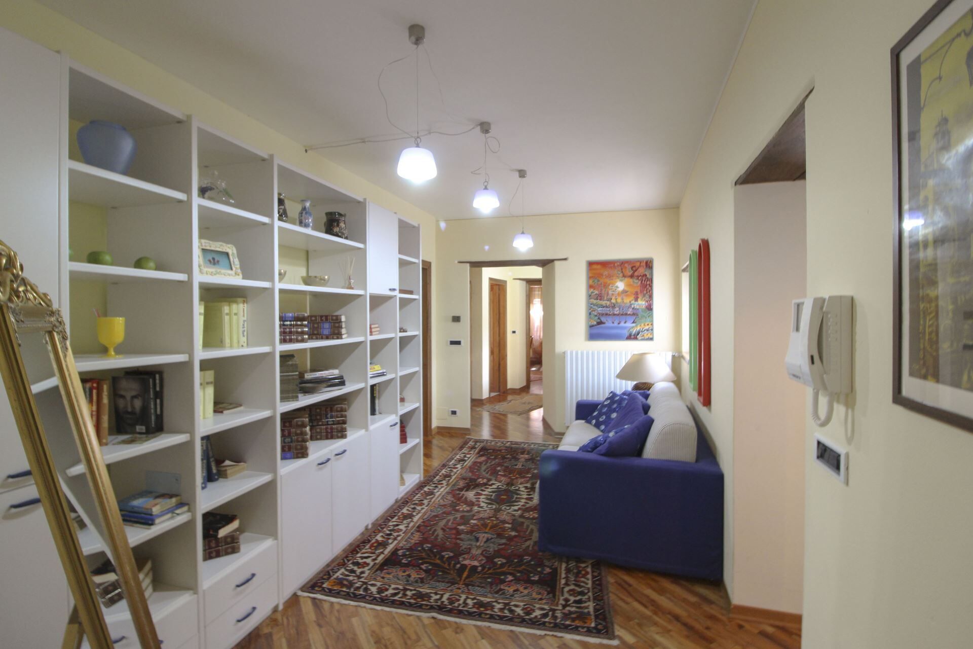 A room with a blue sofa, white shelving units, a patterned rug, and a painting on the wall.