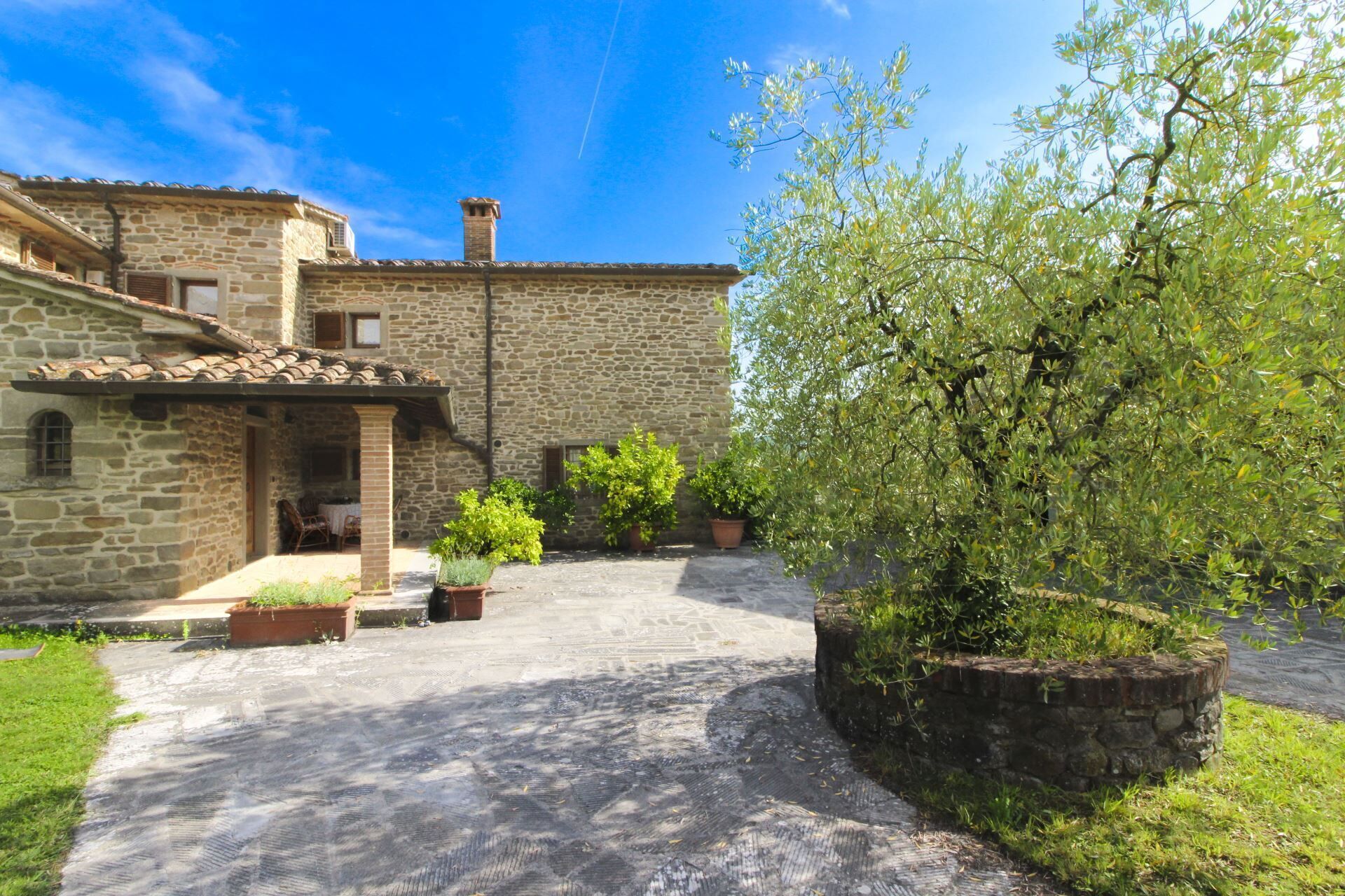 A stone building with a courtyard, potted plants, and a tree.