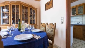 Comedor con una mesa redonda dispuesta para seis comensales, rodeada de sillas de madera con diseños elaborados. Se observa un aparador de madera con puertas de cristal que exhibe vajilla y cristalería.