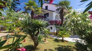 Un edificio de dos plantas con fachada blanca y un balcón con flores rosadas.