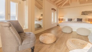 A bedroom with a large bed, a chair, and a round woven ottoman. - Elizabeth House Varenna (Varenna)