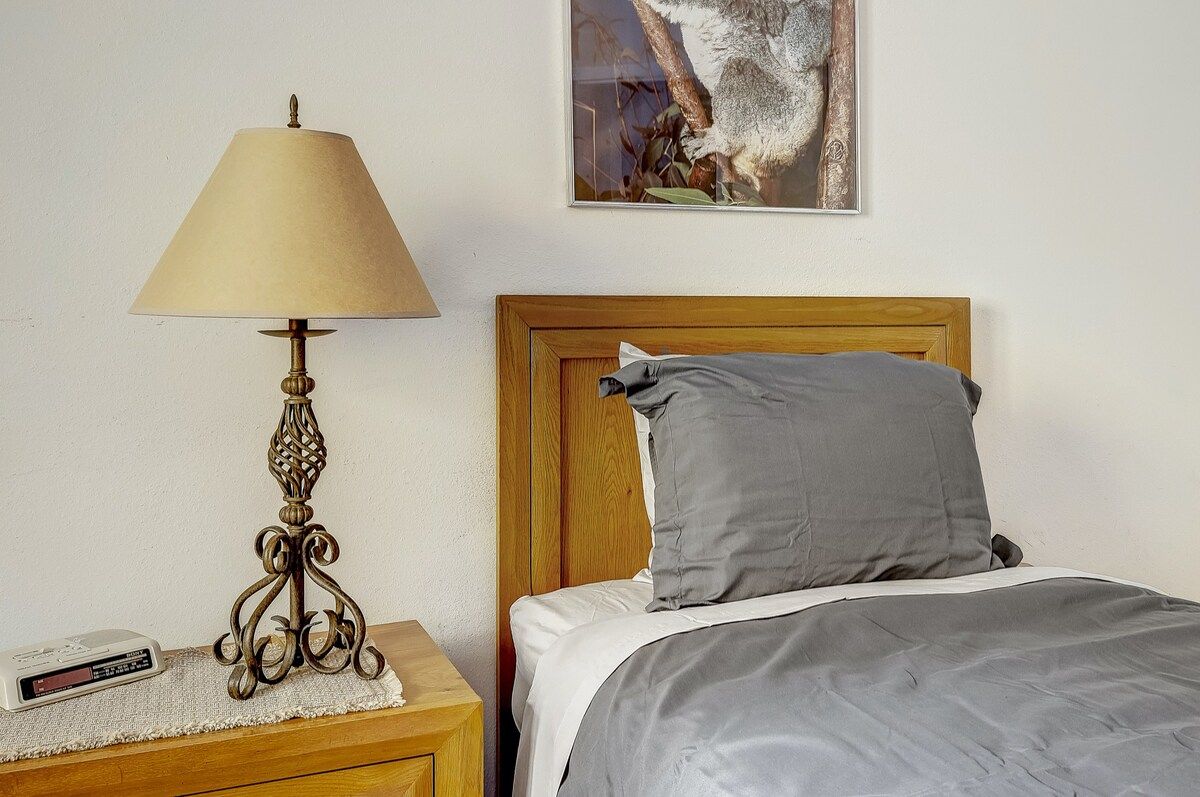 A bed with a wooden headboard, a grey pillow, and a bedside table with a lamp.
