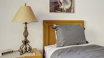 A bed with a wooden headboard, a grey pillow, and a bedside table with a lamp.