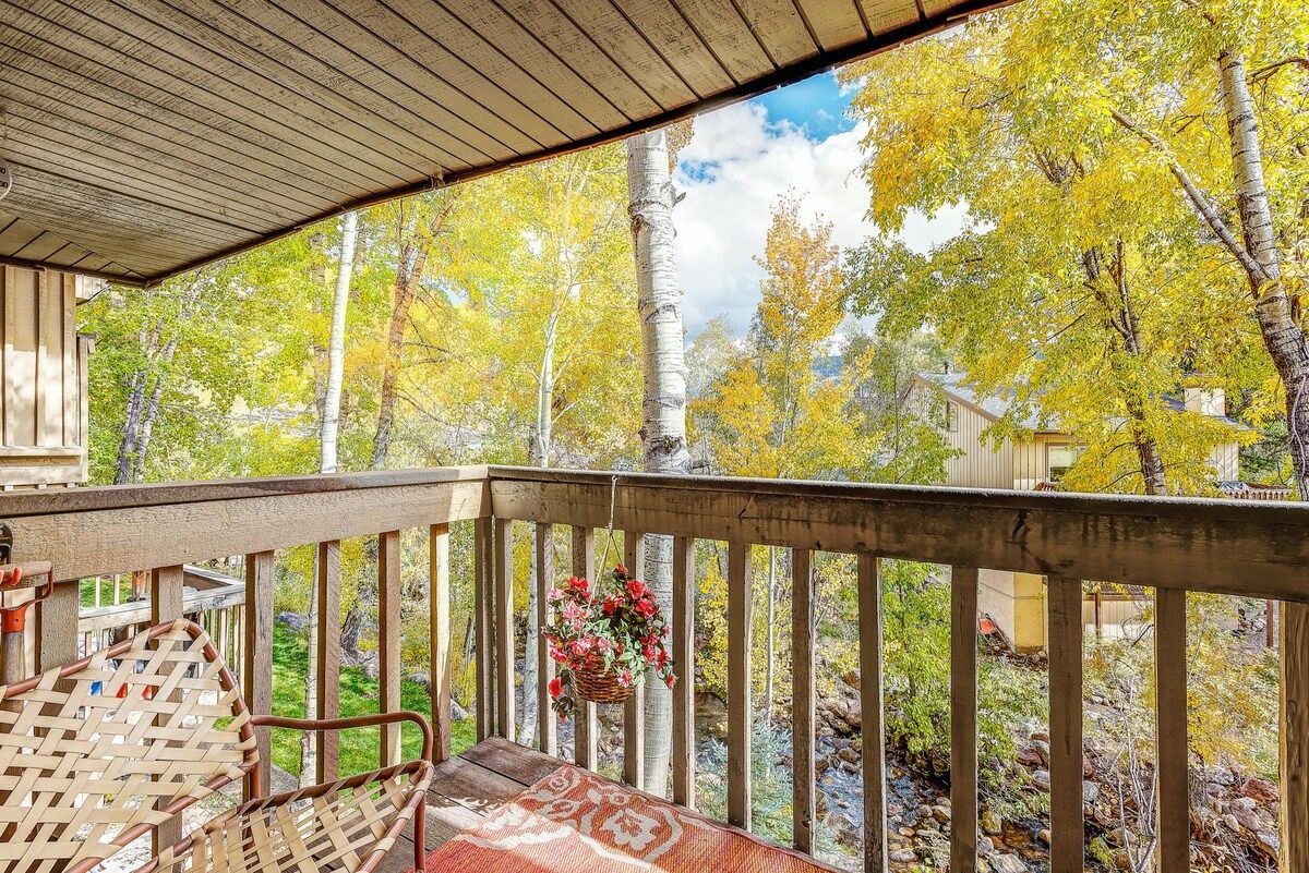 A wooden deck with a railing, a hanging flower basket, and a view of trees with yellow leaves.