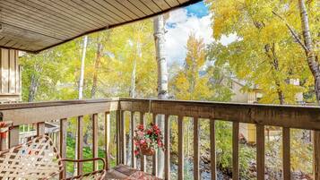 A wooden deck with a railing, a hanging flower basket, and a view of trees with yellow leaves.