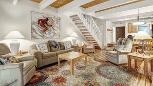 A spacious living room with a staircase, a large abstract painting, and a dining area with a table and chairs.