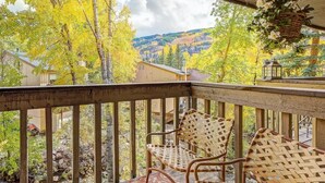 A wooden deck with wicker chairs, a hanging basket, and a view of a mountainous landscape.