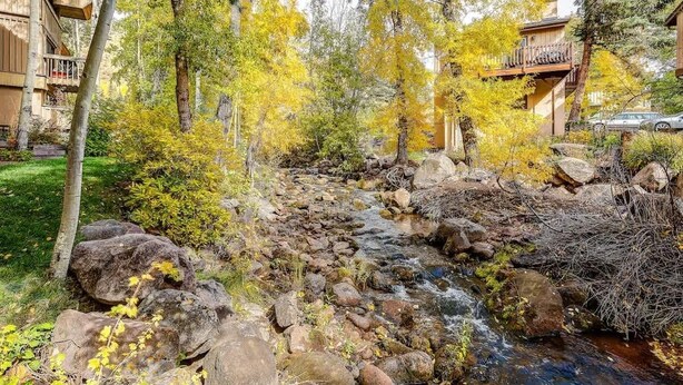 A natural stream with rocks and trees, surrounded by buildings with balconies.