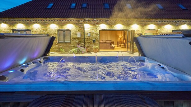 A hot tub with a wooden deck in front of a brick building with a tiled roof.