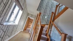 A staircase with wooden railings and a view of a room with a window and patterned wallpaper.