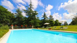 Una piscina blu cristallina con lettini e ombrelloni, immersa nel verde lussureggiante e alberi alti.