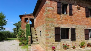 Un edificio rustico in pietra con facciata in mattoni, una scalinata in pietra che conduce a una porta e piante in vaso a terra.