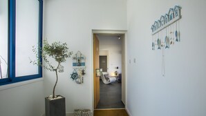 A hallway with a potted plant, a welcome sign, and a view into a room with a bed and a chair. - Protaras Aster Seaside Suite (Protaras)