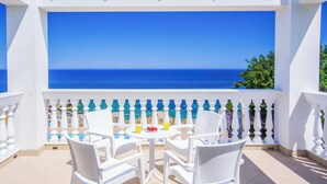 Een balkon met witte rieten meubels, een tafel met eten en drinken, en uitzicht op zee.