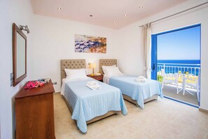 Ein Hotelzimmer mit zwei Betten, einem Holztisch, einem Gemälde und einem Balkon mit Meerblick.
