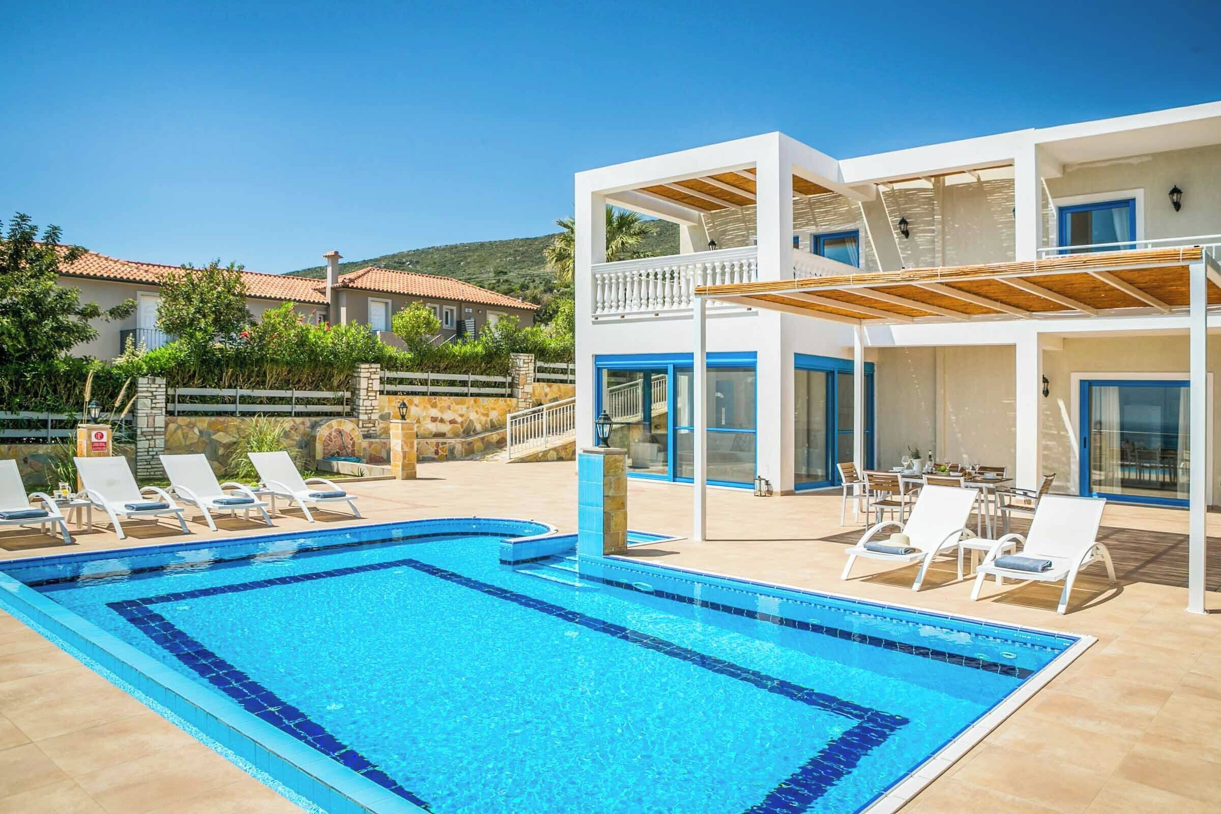 A swimming pool with lounge chairs, a covered outdoor seating area, and a two-story building with a balcony.