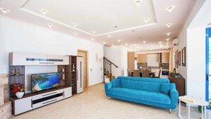 Een ruime woonkamer met een grote televisie, een blauwe bank en een kleine tafel.