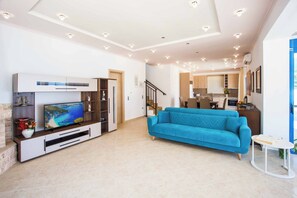 Un salón espacioso con un televisor grande, un sofá azul y una mesita pequeña.