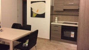A compact kitchen with a dining area, featuring a modern design with a white wall, a large abstract painting, and a tiled backsplash. - Salieri Apartment 2 bedrooms (Latina)