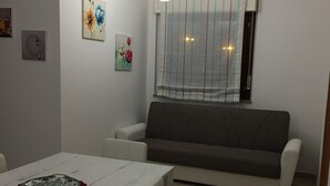 A dining area with a white table, a grey sofa, and a window with striped curtains. - Salieri Apartment 2 bedrooms (Latina)