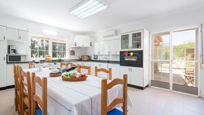 Una cocina amplia con armarios blancos, una mesa de comedor con sillas y vistas al exterior a través de una puerta corrediza de vidrio.