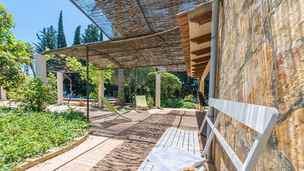Un espacio al aire libre con asientos, una mesa con un tazón de bocadillos y una pérgola que proporciona sombra.