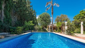 Una piscina azul cristalina rodeada de exuberante vegetación y un edificio tradicional con tejado de azulejos.
