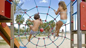 Kinder spielen auf einer Seilnetz-Struktur in einem Strandspielplatz.