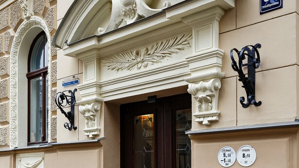 A building with ornate architectural details, a dark wooden door, and a sign indicating the address.
