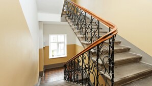 A staircase with ornate black metal railings and a wooden handrail, leading to a landing with a window.
