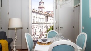 A dining area with a table set for two, chairs, a lamp, and a view of a building with a clock tower.