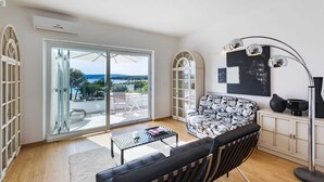 Een moderne woonkamer met een bank, een salontafel en een uitzicht op de omgeving door grote glazen deuren.