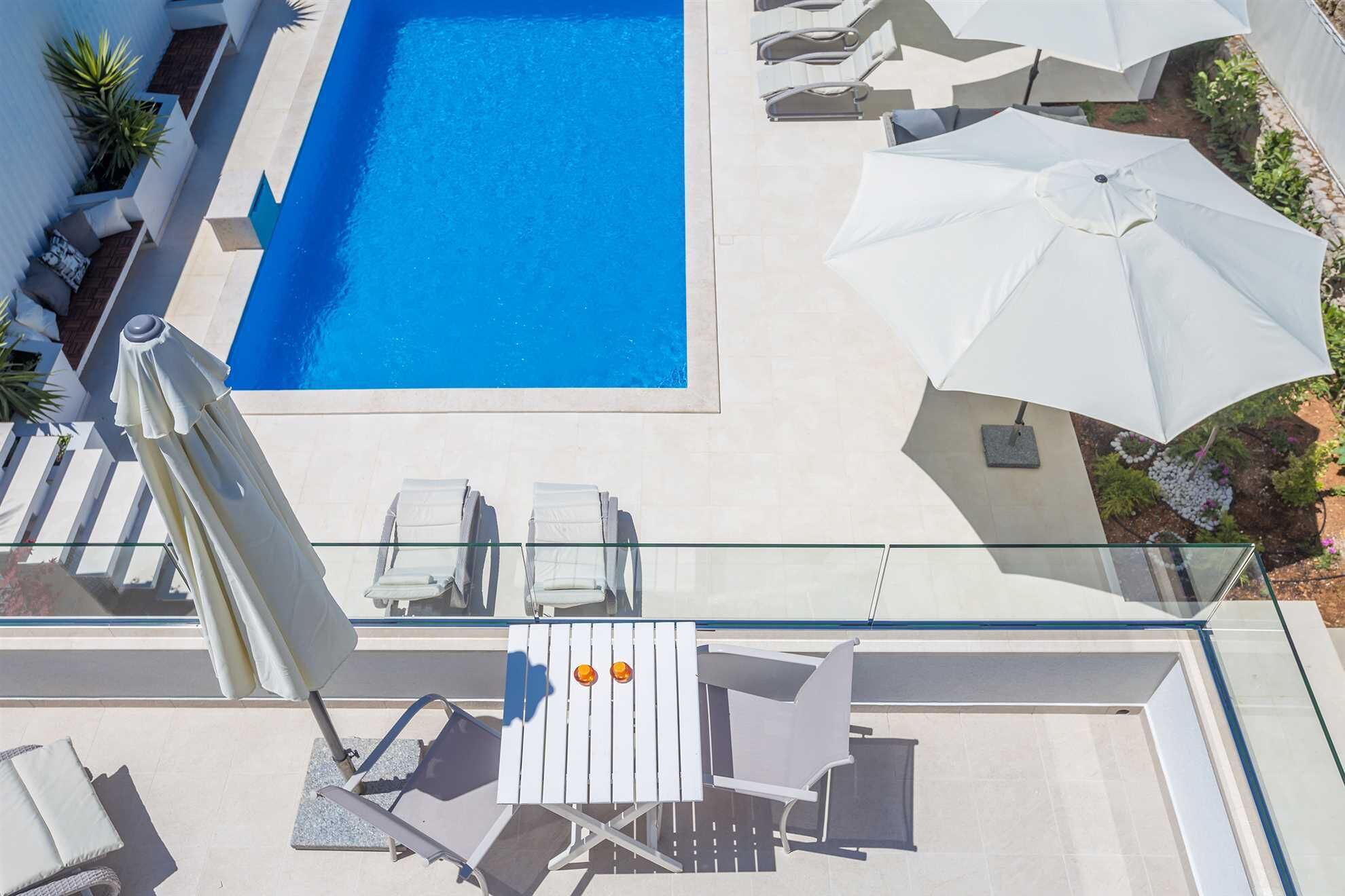 A rooftop pool area with a clear blue pool, white lounge chairs, and umbrellas.