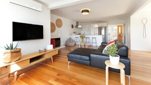Una sala moderna con un televisor de pantalla plana, piso de madera, un sofá de cuero negro y una mesita con una planta.