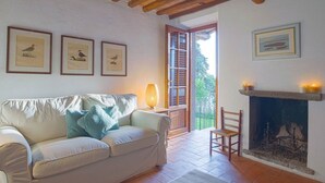 A cozy living room with a white sofa, framed bird illustrations, a fireplace, and a wooden ceiling. - Santa Lucia Suite, apartment with lovely view over the shore (Santa Lucia)