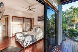 A modern bedroom with a large bed, sliding glass door to a balcony, and a ceiling fan.