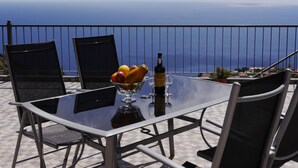 Un tavolo con una bottiglia di vino, bicchieri e una ciotola di frutta su un balcone vista mare.
