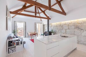 A modern kitchen with a marble countertop, a stone wall, and wooden beams on the ceiling. - Boutique Rentals - HIDDEN TREASURE: 2-Bedroom Apartment with Balcony and Views of the Douro River   (Porto)