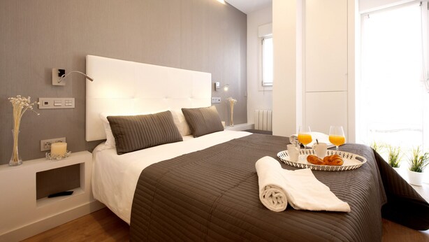 Una habitación de hotel moderna con una cama grande, mesitas de noche, una bandeja con desayuno y una ventana con luz natural.