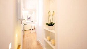 Un pasillo con una puerta blanca, un banco blanco, una planta en maceta y dos velas sobre estantes.