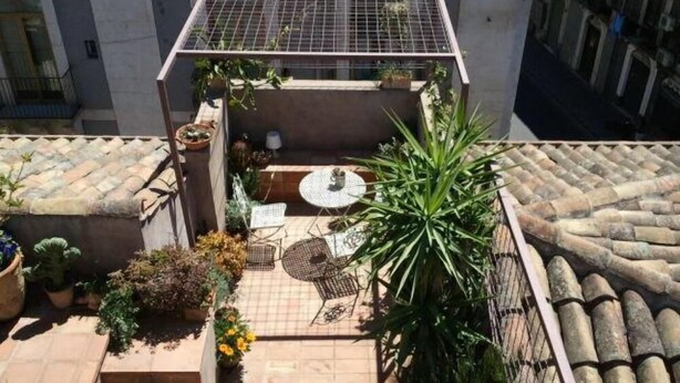Une terrasse sur le toit, avec une table et des chaises, entourée de plantes en pot et d’un petit espace aménagé en jardin.
