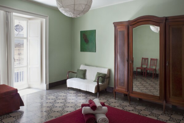 A room with a white sofa, a wooden wardrobe, a red rug, and a green painting on the wall.