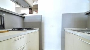 Une cuisine de taille réduite, équipée d’une cuisinière à gaz, de meubles blancs et d’un petit plan de travail.