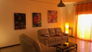 A living room with a sofa, armchair, and coffee table. There are two wall-mounted paintings and a floor lamp. - Paolo Suite in via Parioli in Gela (Gela)