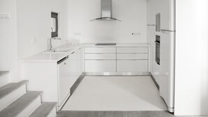 Une cuisine moderne avec des meubles blancs, une hotte en acier inoxydable, un four encastré et un réfrigérateur.