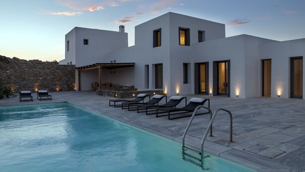 Une villa moderne dotée d’une piscine, d’un espace salon extérieur et d’un mur en pierre servant de décor.
