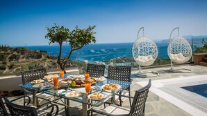 Ein Tisch ist für eine Mahlzeit gedeckt, mit Blick auf das Meer, zwei Hängesessel und ein kleiner Baum.