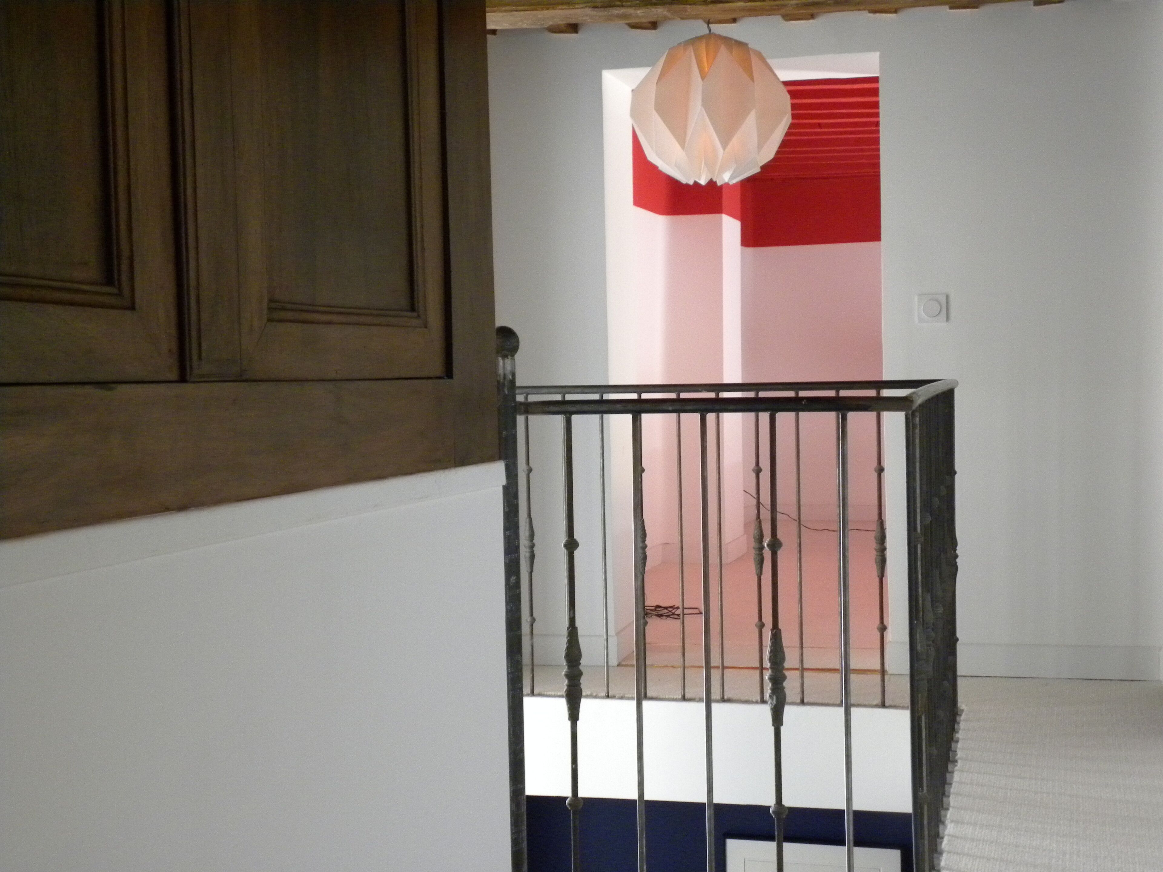 Une pièce avec une porte en bois, une rambarde en métal et une fenêtre à rayures rouges et blanches.