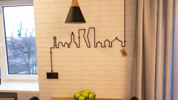 Un comedor con una mesa de madera, dos sillas negras, una lámpara colgante negra y un cuadro mural con vista a la ciudad.